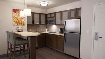 A modern kitchen with wooden cabinets, a stainless steel refrigerator, a microwave, and a sink. There is a dining table with a chair and a pendant light.