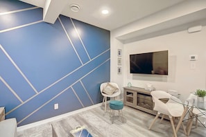 A modern living room with a blue accent wall, a flat-screen TV, a dining area with chairs, and a wooden cabinet.