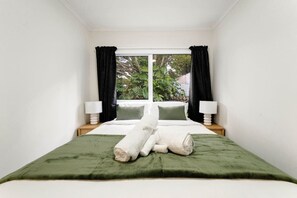 A bedroom with a bed, two bedside lamps, a window with curtains, and a view of greenery outside. - Sandringham 2BR Haven near Eden Park with Air-con (Auckland Central Suburbs)