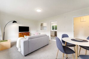 A modern living room with a sofa, a TV, a dining table with chairs, and a kitchen in the background. - Sandringham 2BR Haven near Eden Park with Air-con (Auckland Central Suburbs)