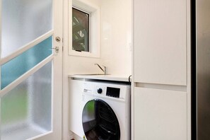 A compact laundry room with a washing machine, a small window, and a door. - Sandringham 2BR Haven near Eden Park with Air-con (Auckland Central Suburbs)