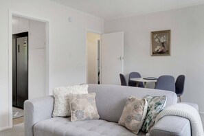 A modern living room with a grey sofa, floral cushions, a dining table with chairs, and a painting on the wall. - Sandringham 2BR Haven near Eden Park with Air-con (Auckland Central Suburbs)