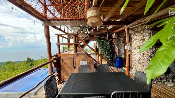 A wooden outdoor seating area with a table and chairs, overlooking a body of water.