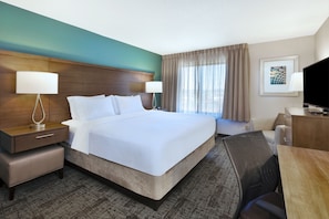 A hotel room with a large bed, a desk, a chair, a TV, and a window with curtains.