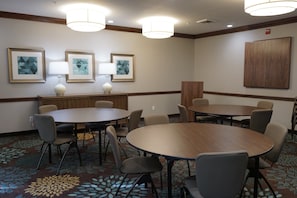 A conference room with round tables and chairs, framed artwork on the walls, and a patterned carpet.