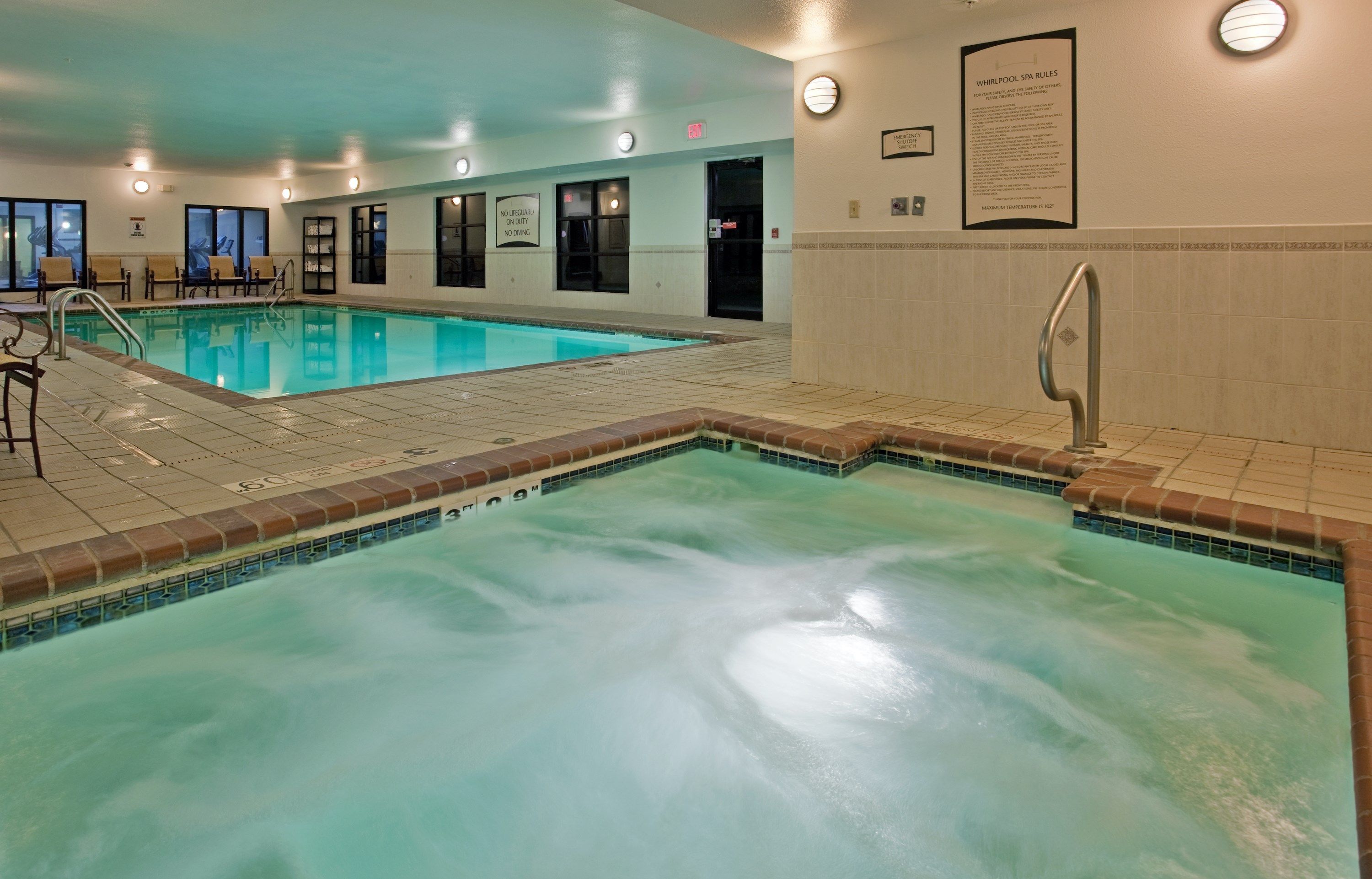 Piscina interna com água cristalina, deck revestido com azulejos e uma placa com as regras do spa.