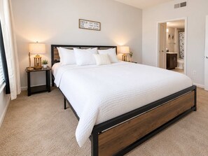 A bedroom with a large bed, two bedside tables with lamps, a wall-mounted sign, and a door leading to a bathroom. - The little Havana (Austin)