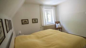 Una camera da letto con un letto, una sedia, una finestra con tende e quadri appesi al muro.
