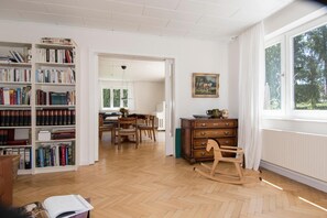 Una habitación amplia con una gran estantería, un comedor y un ventanal con vistas a la vegetación.