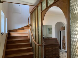 Una escalera de madera con barandilla que lleva a una habitación con un aparador de madera y una cesta colgada en la pared.