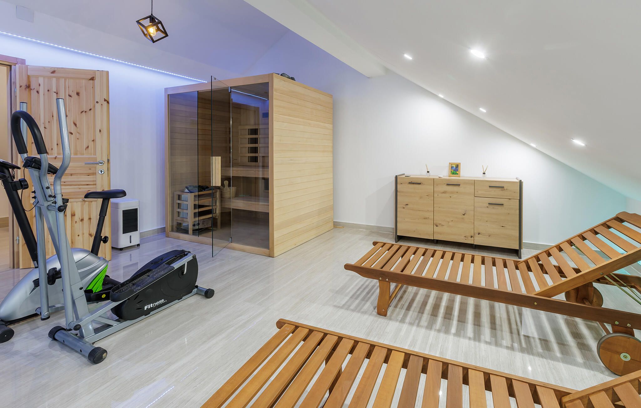 Une chambre moderne dotée d’un ventilateur de plafond, d’un tapis de course, d’une armoire en bois et d’une porte en verre donnant sur un placard.
