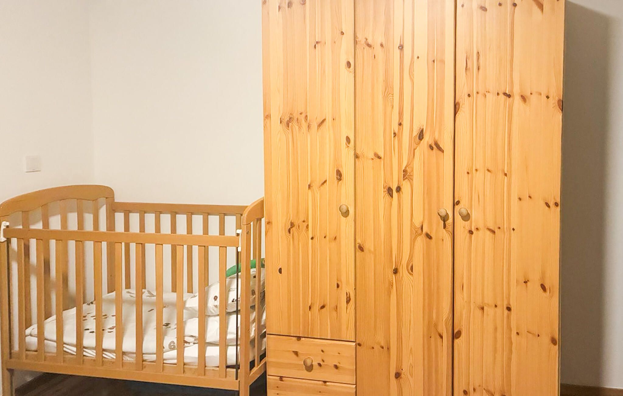 Un berceau en bois doté d’un tiroir, placé à côté d’une armoire en bois dont les poignées sont apparentes.