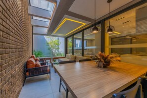 Un intérieur moderne avec une longue table à manger, un mur en briques et une vue sur la verdure à l’extérieur.