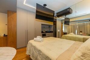 Une chambre d’hôtel comprenant un lit, un bureau, un miroir, une kitchenette et une salle de bain.