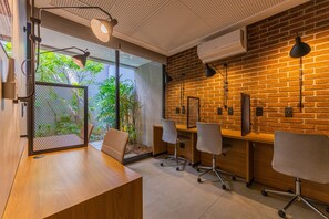 A modern office space with a wooden desk, two office chairs, a brick wall, and a view of greenery through a glass partition. - Studio with Pool and Gym 400m from Paulista Avenue (São Paulo)