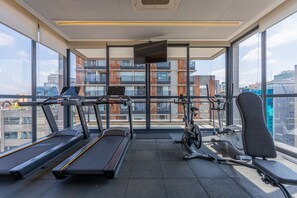 A gym with treadmills, a stationary bike, and a rowing machine, with large windows offering a city view. - Studio with Pool and Gym 400m from Paulista Avenue (São Paulo)