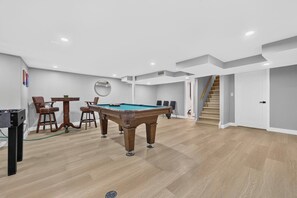 Ein modernes Wohnzimmer mit Billardtisch, einem Essbereich mit Stühlen und einer Treppe zu einer oberen Ebene.