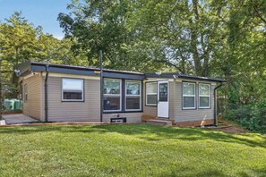 A single-story mobile home with a front porch, a small attached garage, and a fenced yard. - Modern Waterfront Cottage on Grand River | 4BR (Haldimand)