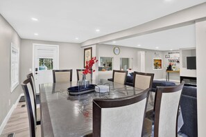 A dining area with a glass-top table, chairs, and a vase with red flowers. - Modern Waterfront Cottage on Grand River | 4BR (Haldimand)