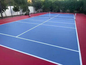 Ein Tennisplatz mit Netz, umgeben von roter und blauer Belag, mit Bäumen im Hintergrund.
