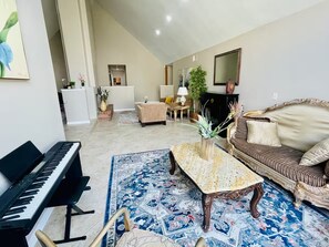 Ein Wohnzimmer mit einem Klavier, einem gemusterten Teppich, einer Couch und einem Couchtisch.