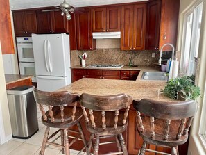 Eine Küche mit Holzausstattung, einem weißen Kühlschrank, einer Arbeitsplatte aus Granit und einem Barhocker.