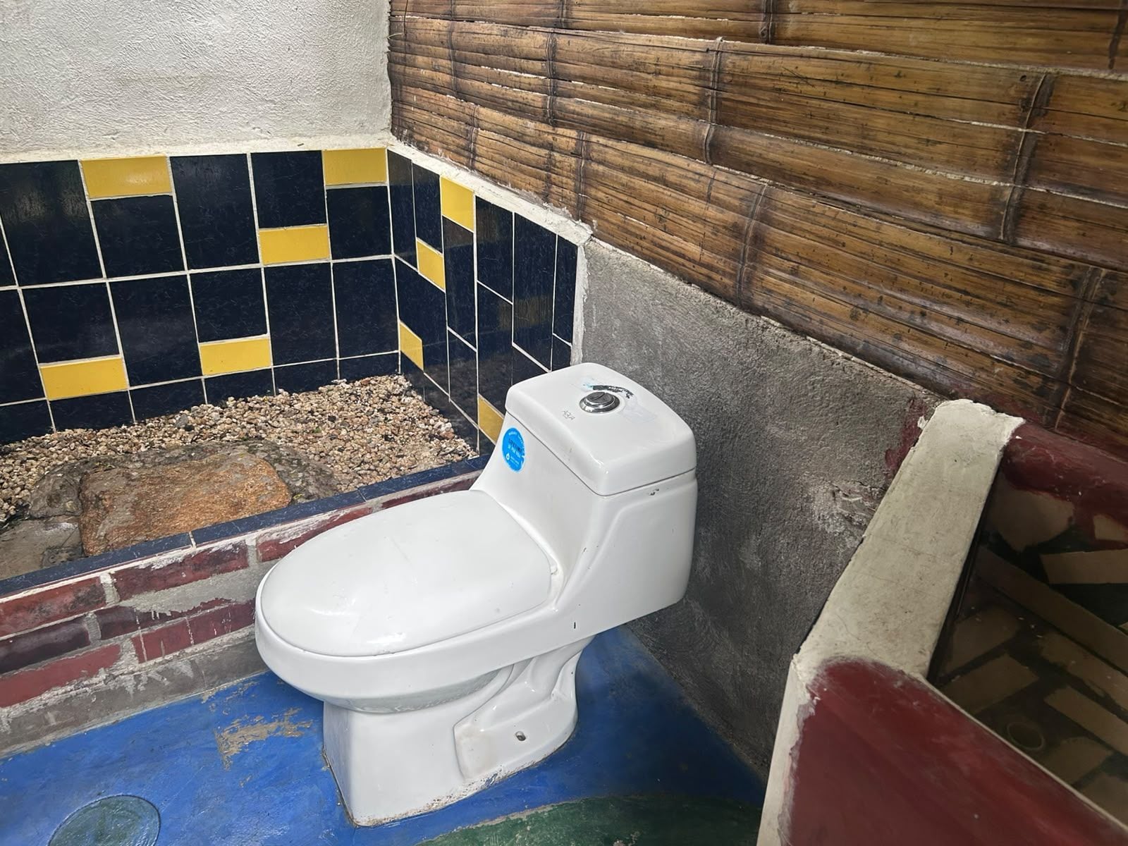 Un inodoro con asiento y tanque blancos, ubicado junto a una pared con diseño de baldosas negras y amarillas.