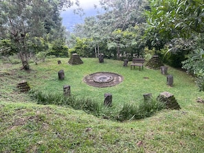 A circular stone structure surrounded by grass and trees, with a bench and stone posts. - Tonkiri Sanctuary (Alotenango)
