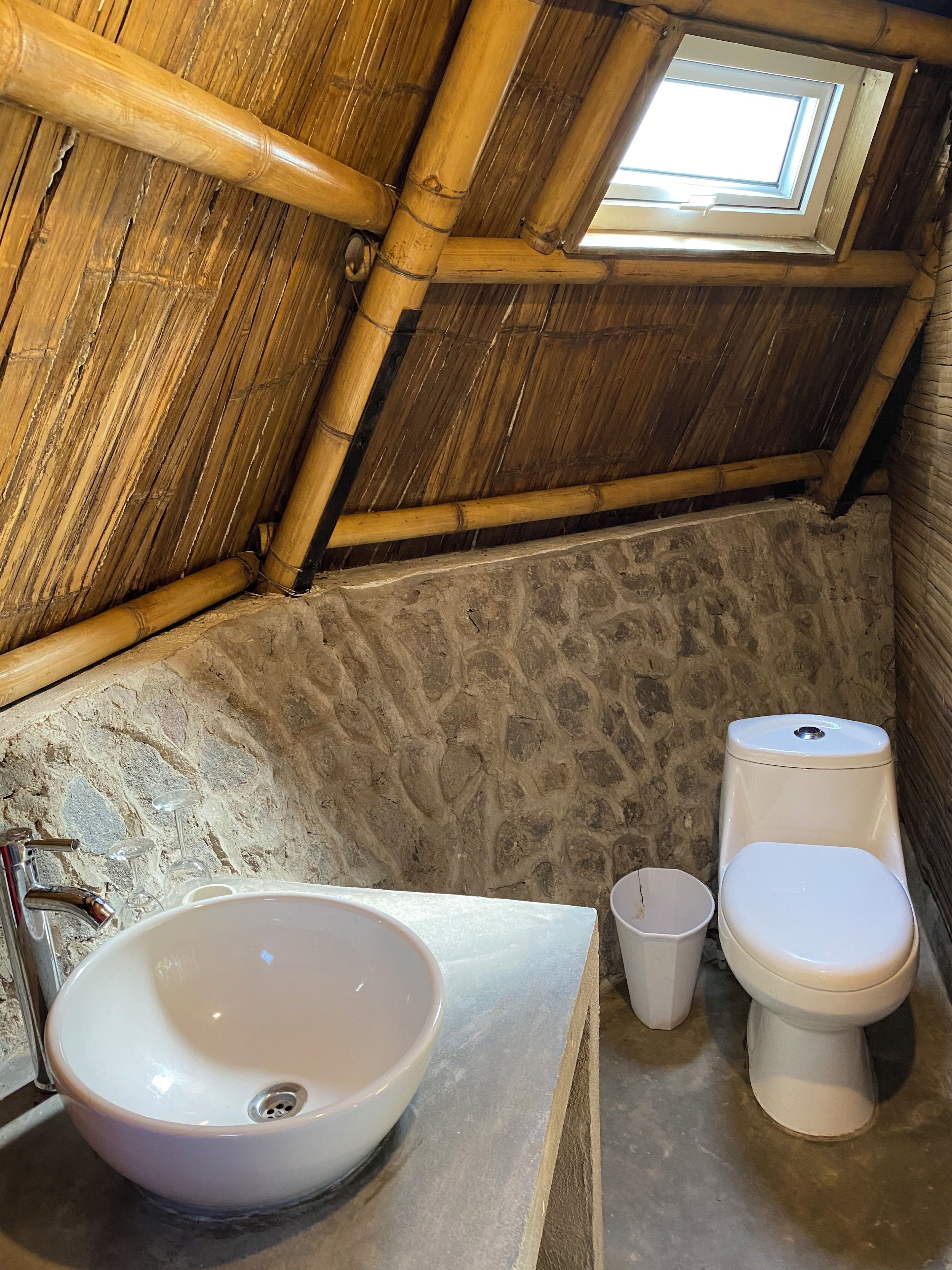 A bathroom with a bamboo ceiling, a stone wall, a white sink, and a toilet.