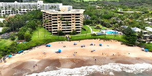 Ein Strandhotel mit mehreren Etagen, einem Pool und einem Sandstrandabschnitt mit Sonnenschirmen.