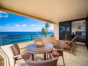 Ein Balkon mit rundem Tisch und Korbstühlen, der Blick auf ein klares, blaues Meer und Palmen freigibt.