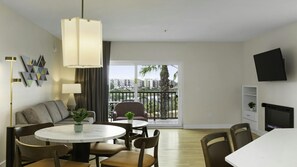 Un salon moderne avec balcon, un coin repas et un téléviseur fixé au mur.