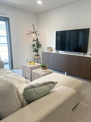 A modern living room with a sofa, a television, decorative plants, and a patterned side table. - Cabanas de Tavira Strand Apartment (Tavira)