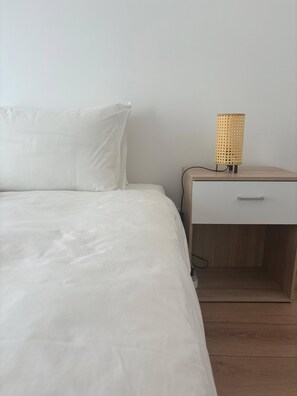 A bed with white bedding, a nightstand with a woven lamp, and a drawer. - Cabanas de Tavira Strand Apartment (Tavira)