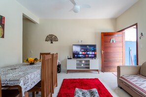 Una sala de estar con televisor, una mesa de comedor con sillas, un tapete rojo y una puerta de madera.