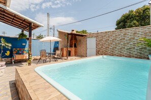 A swimming pool with a tiled deck, a brick wall, and a pergola with a table and chairs. - Casa com Piscina Privativa no Calif Rnia (Cabo Frio)
