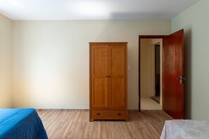 A room with a wooden wardrobe, a bed with a blue cover, and a door leading to another room. - Casa com Piscina Privativa no Calif Rnia (Cabo Frio)
