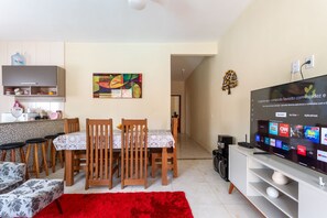 A modern living room with a dining area, a flat-screen TV, and a kitchen in the background. - Casa com Piscina Privativa no Calif Rnia (Cabo Frio)