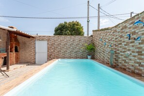 A rectangular swimming pool with a brick wall on one side and a white door on the other. - Casa com Piscina Privativa no Calif Rnia (Cabo Frio)