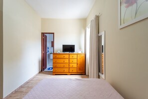 A bedroom with a bed, a wooden dresser, a television, and a door leading to another room. - Casa com Piscina Privativa no Calif Rnia (Cabo Frio)