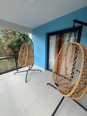 A balcony with two wicker chairs, a glass door, and a view of greenery. - The Palmier Bleu Duplex! (Rivière-Salée)