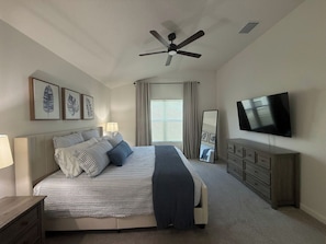A bedroom with a bed, a ceiling fan, a television, a dresser, and a window with curtains. - Brand-New Stylish 2BR Villa with Golf Cart in The Villages (The Villages)