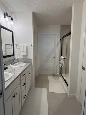 A bathroom with two sinks, a large mirror, a shower with glass doors, and a white door. - Brand-New Stylish 2BR Villa with Golf Cart in The Villages (The Villages)