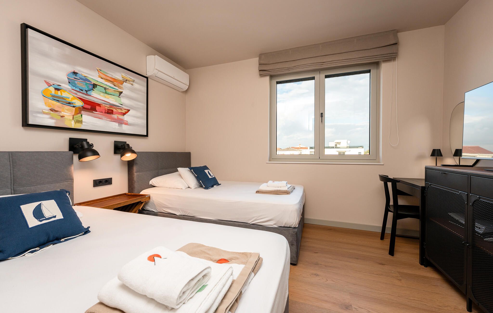 Ein Hotelzimmer mit zwei Betten, einem Schreibtisch, einem Stuhl, einem Fernseher und einem Fenster mit Blick.
