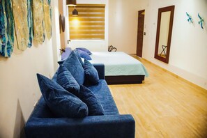 A room with a blue sofa, a bed, and a wooden floor. There is a window with blinds and a door with a mirror. - Ancla Baja Living 5 (La Paz)