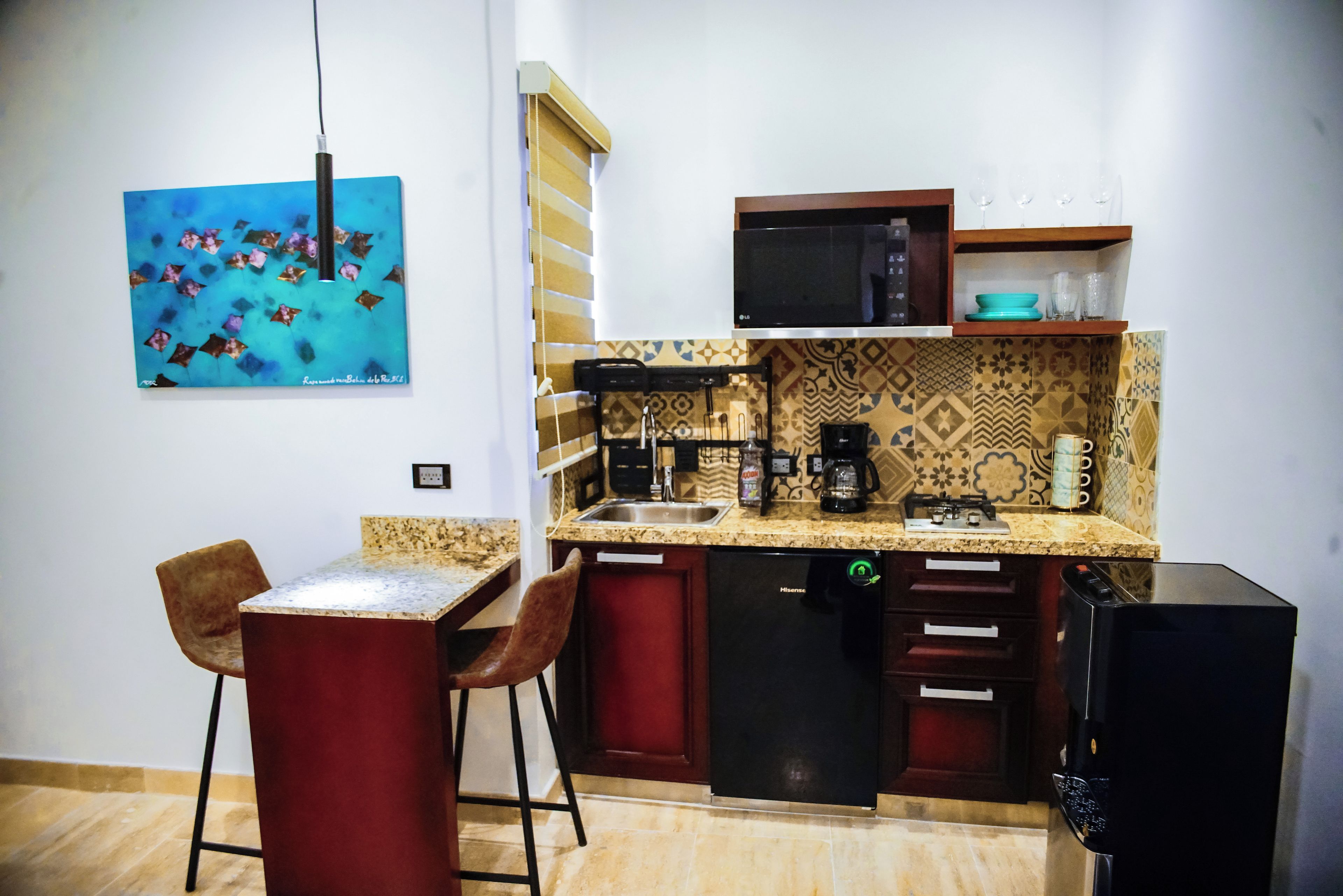 Cocina compacta con microondas, cafetera y lavabo. Hay dos taburetes y una pequeña mesa.