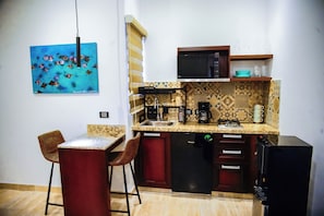 A compact kitchen with a microwave, coffee maker, and a sink. There are two stools and a small table. - Ancla Baja Living 5 (La Paz)