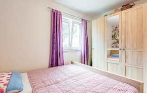 Ein Schlafzimmer mit einem Bett, einem Fenster mit violetten Vorhängen und einem Holzschrank.