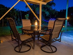 A round table with four chairs, a lit candle, and a starry night sky in the background. - Peaceful 2BR Cottage in Keaau | Volcano & Beaches (Keaau)