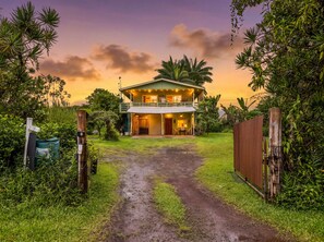 A two-story house with a covered porch and a dirt path leading to the entrance. - Peaceful 2BR Cottage in Keaau | Volcano & Beaches (Keaau)